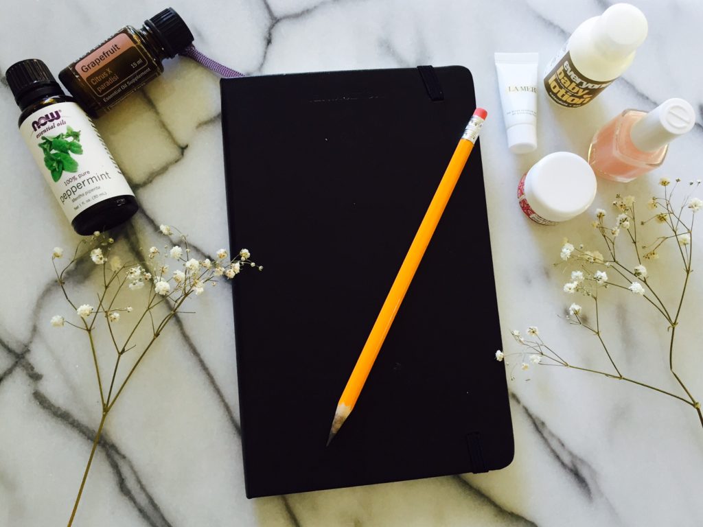 black notebook with pencil on top surrounded with beauty and health products 