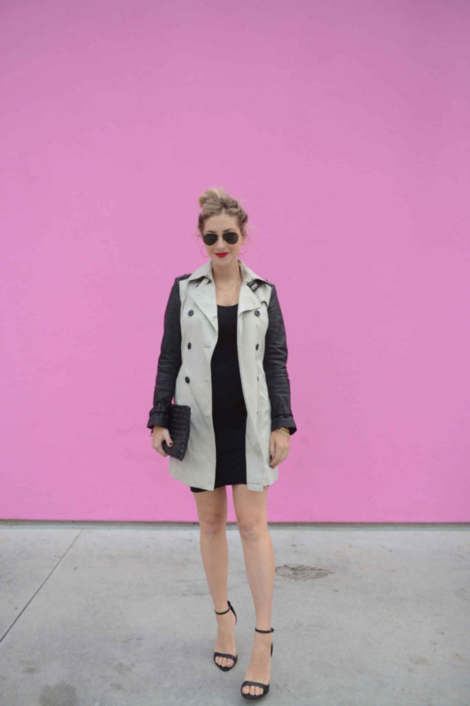 woman wearing coat and black dress standing in front of a pink wall