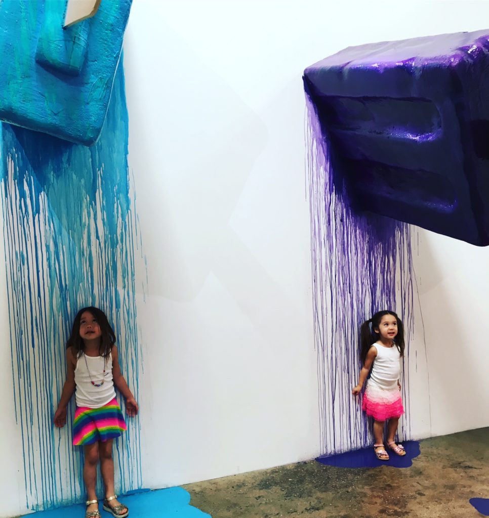 two kids leaning on a white wall with ice cream melting on it